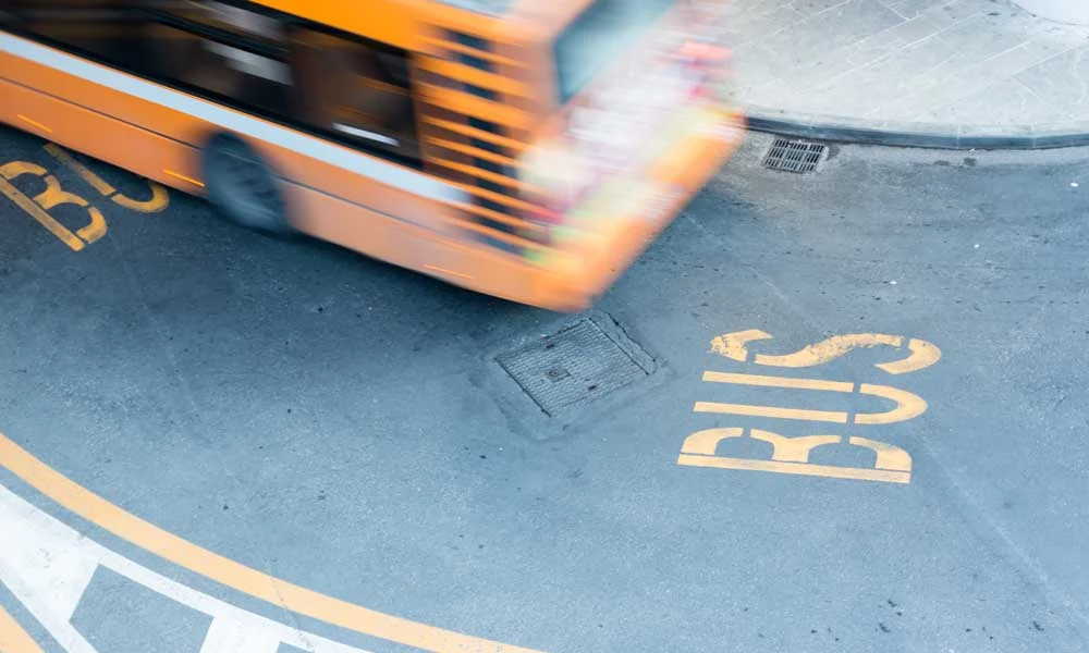 Orange City Bus Turning Across a Street, with a Large Yellow'BUS' stencil painted on the pavement nearby.